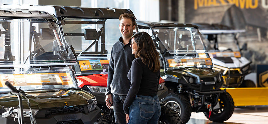 Man and woman standing in front of off-road vehicles in a showroom.