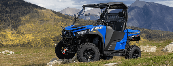 Blue and black UTV on a grassy hill with mountains in the background